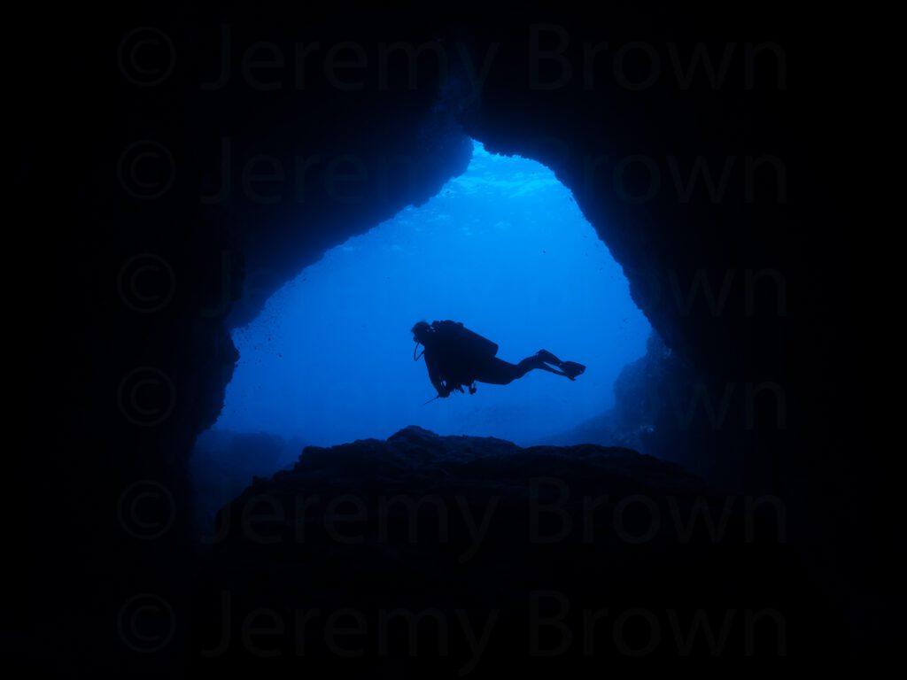 diver silhouetted in entrance of wolang cave. alor archipelago,